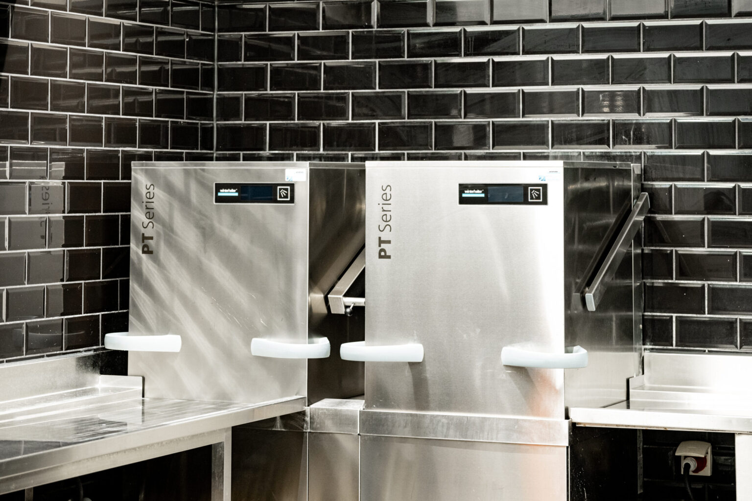 Zwei professionelle PT Series Spülmaschinen in einer professionellen Gastronomieküche. FHE GASTRO ist Ihr Partner für erstklassige Gastro-Geräte und Einrichtungen, die Effizienz und Langlebigkeit bieten.