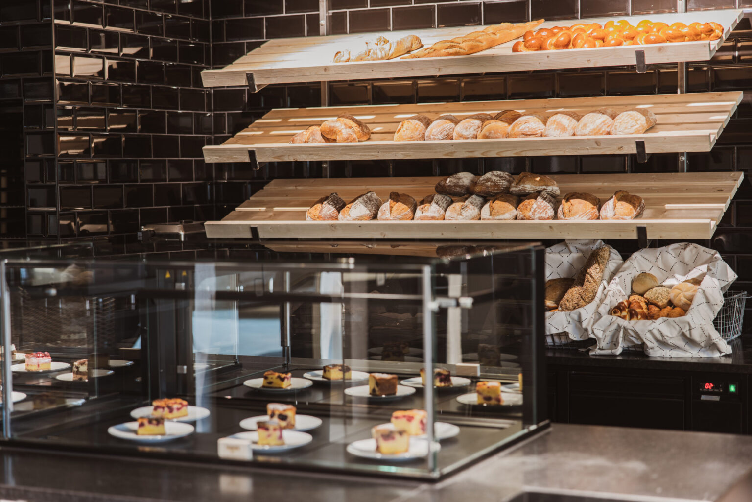Ein moderner Bäckereibereich mit verschiedenen Backwaren wie Croissants, Brötchen und Kuchen, die in eleganten Vitrinen präsentiert werden. FHE GASTRO ist der Hersteller und Lieferant dieser hochwertigen Möbel und Geräte, die für eine ansprechende und effiziente Präsentation von Speisen sorgen.