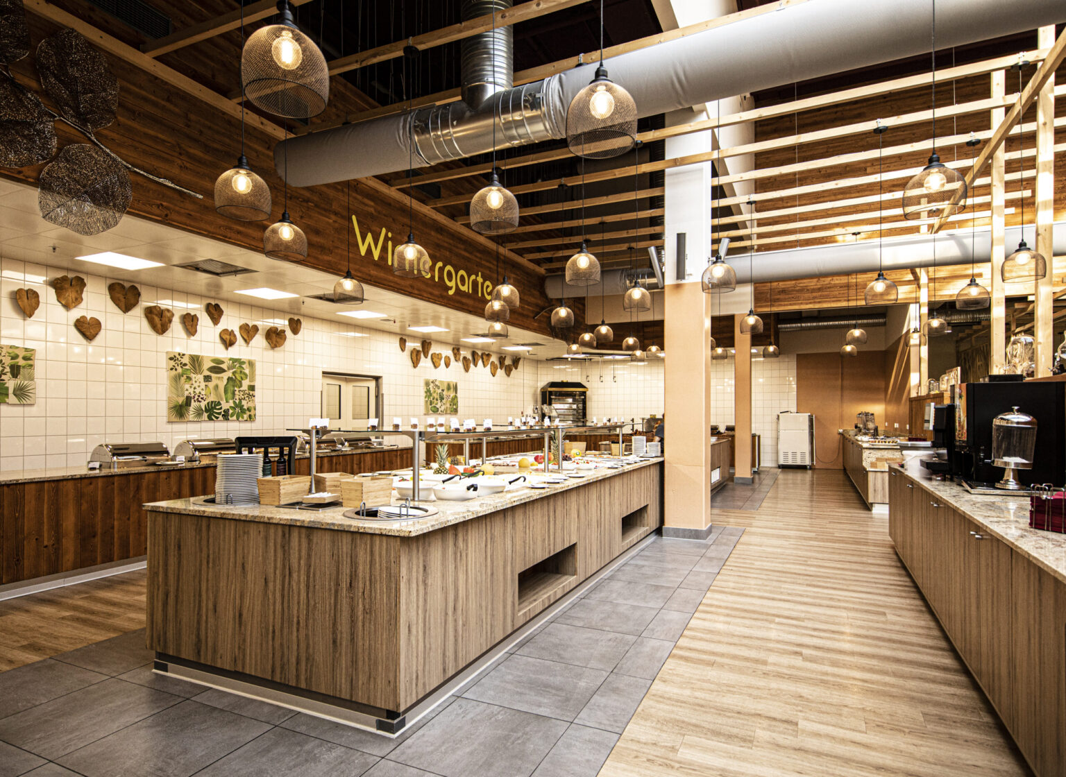 Centerparcs_Leutkirch_19BU Gemütlich gestalteter Free-Flow-Bereich von FHE GASTRO mit Holzelementen und dekorativen Hängelampen. In der Mitte ein großzügiges Buffet mit warmen Holzverkleidungen und moderner Beleuchtung.