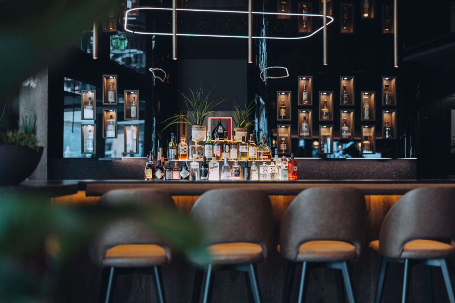 Fernblick_Bartholomäberg 2024 (5) Stilvolle Bar von FHE GASTRO mit modernem Design und gut sortierter Auswahl an Spirituosen, beleuchtet durch dezente Wandregale und eine elegante Deckenbeleuchtung. Im Vordergrund sind bequeme Barstühle zu sehen.