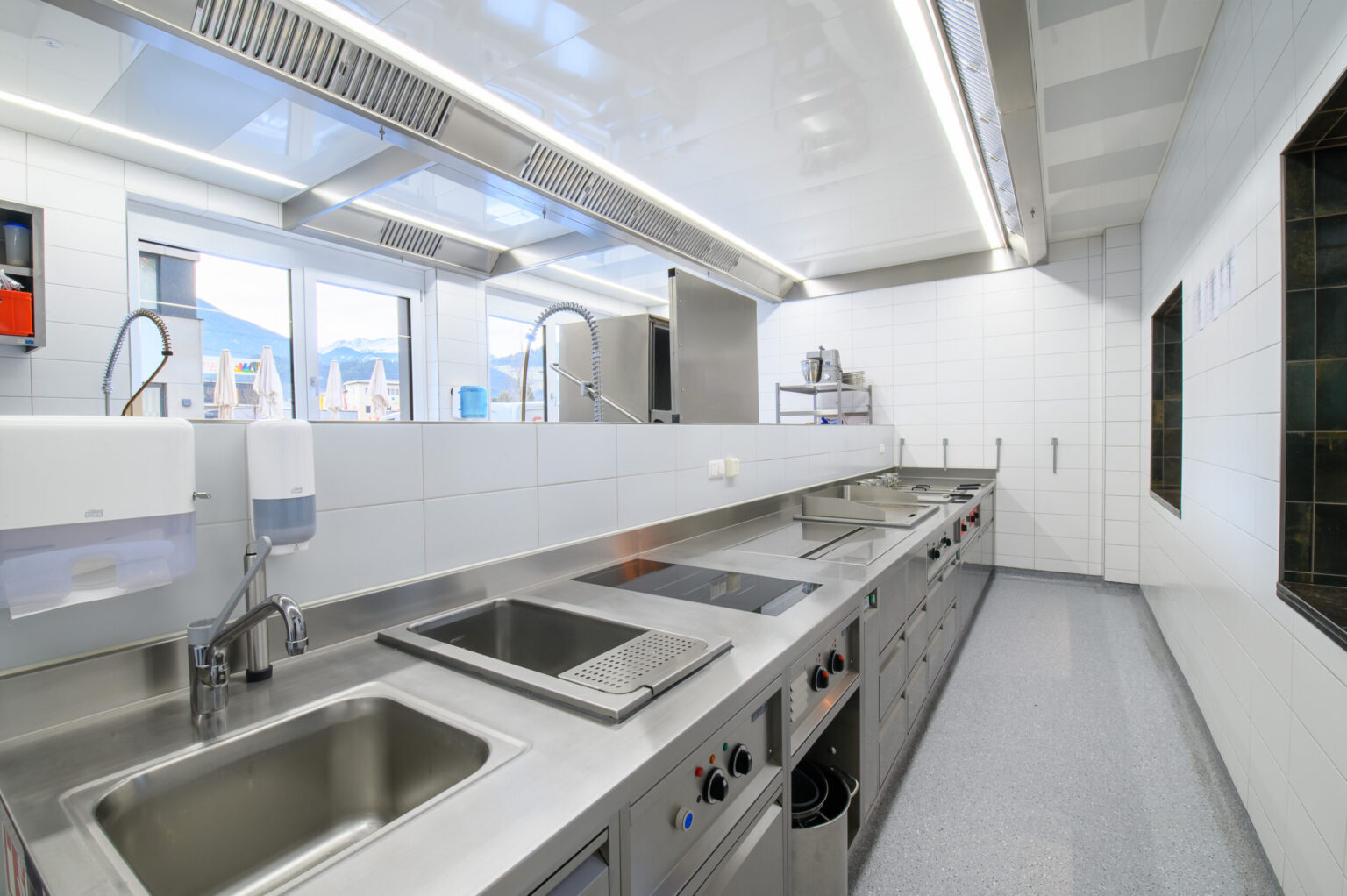 Blick auf eine moderne Gastronomieküche mit Edelstahl-Arbeitsflächen, ideal für die Zubereitung von Speisen in Restaurants und Hotels. Diese professionelle Ausstattung wurde von FHE GASTRO geliefert und sorgt für eine effiziente und hygienische Arbeitsumgebung.