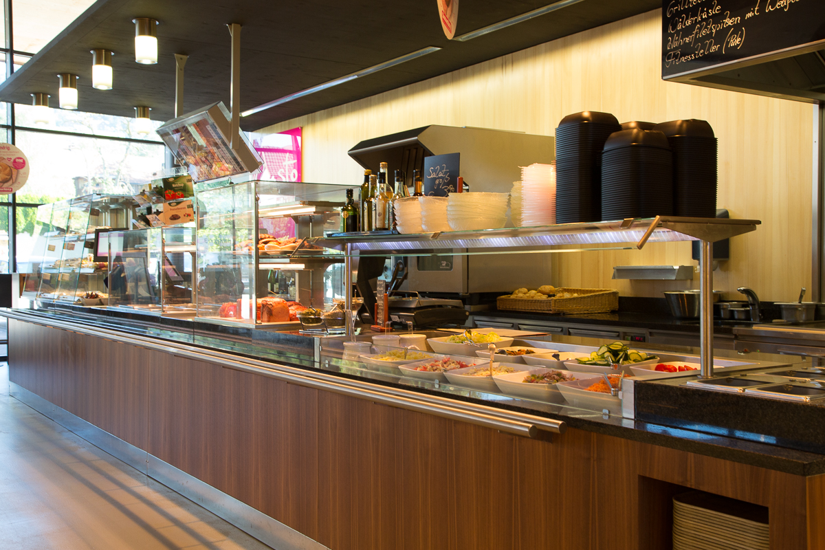Imbissbereich im Sutterlüty Supermarkt mit einer Vielzahl von frisch zubereiteten Lebensmitteln und Salaten in modernen Theken. FHE GASTRO bietet maßgeschneiderte Lösungen für Gastronomiebetriebe wie Sutterlüty, die auf hochwertige Kücheneinrichtungen setzen.