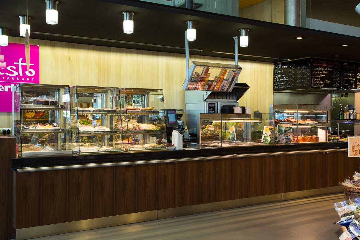 Moderne Selbstbedienungsstation im Sutterlüty Supermarkt mit frischen Angeboten und klar strukturierten Vitrinen, die Produkte wie Sandwiches und Salate präsentieren. FHE GASTRO liefert innovative Gastronomiekonzepte für Supermärkte und ähnliche Betriebe.