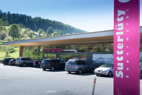 Sutterlüty Mäder 2017 (4) Außenansicht des Sutterlüty Supermarktes in Mäder mit modernen, transparenten Fassaden und einem klaren Markenzeichen. Der Supermarkt setzt auf innovative Verkaufsflächen und eine einladende Architektur.