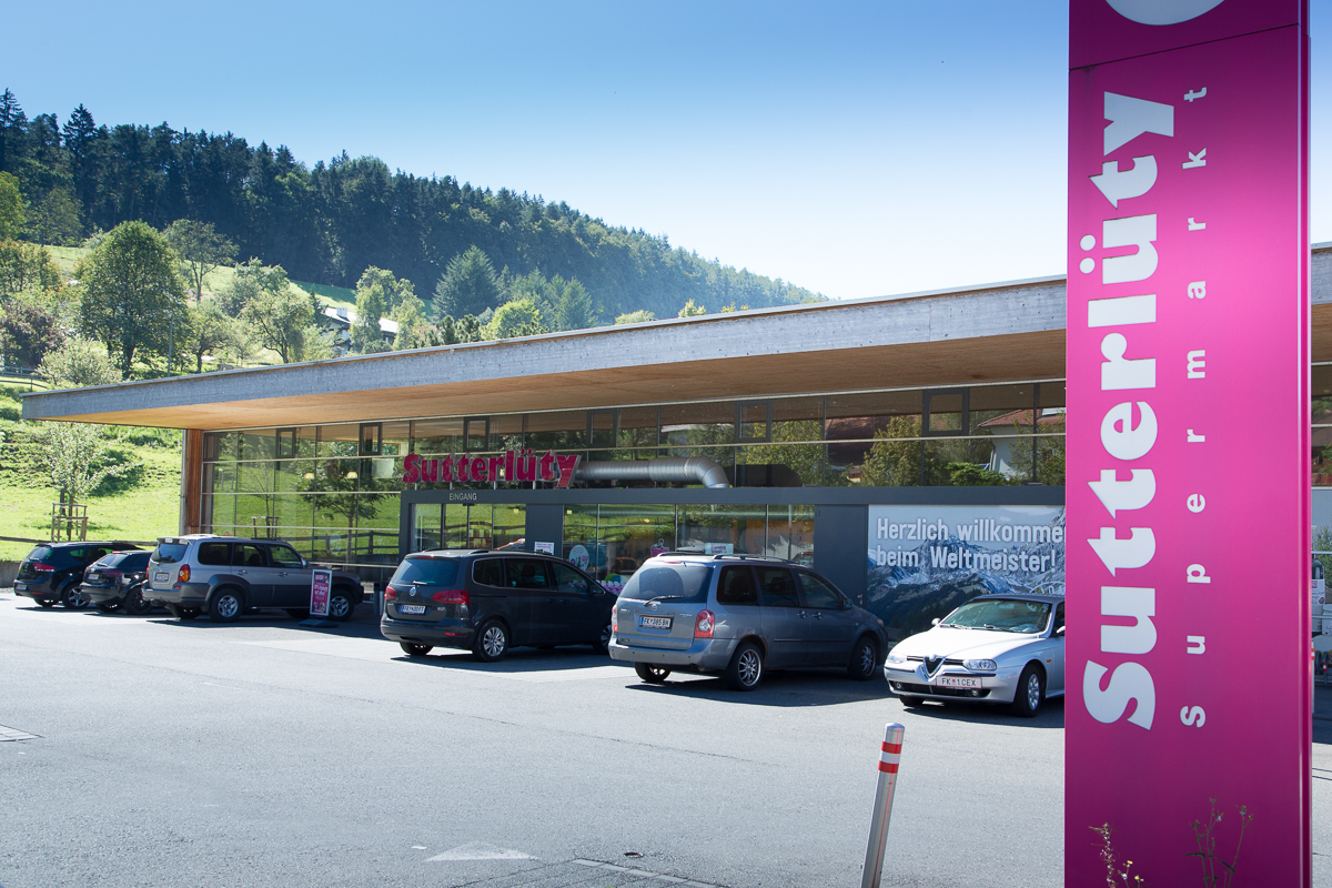 Außenansicht des Sutterlüty Supermarktes in Mäder mit modernen, transparenten Fassaden und einem klaren Markenzeichen. Der Supermarkt setzt auf innovative Verkaufsflächen und eine einladende Architektur.