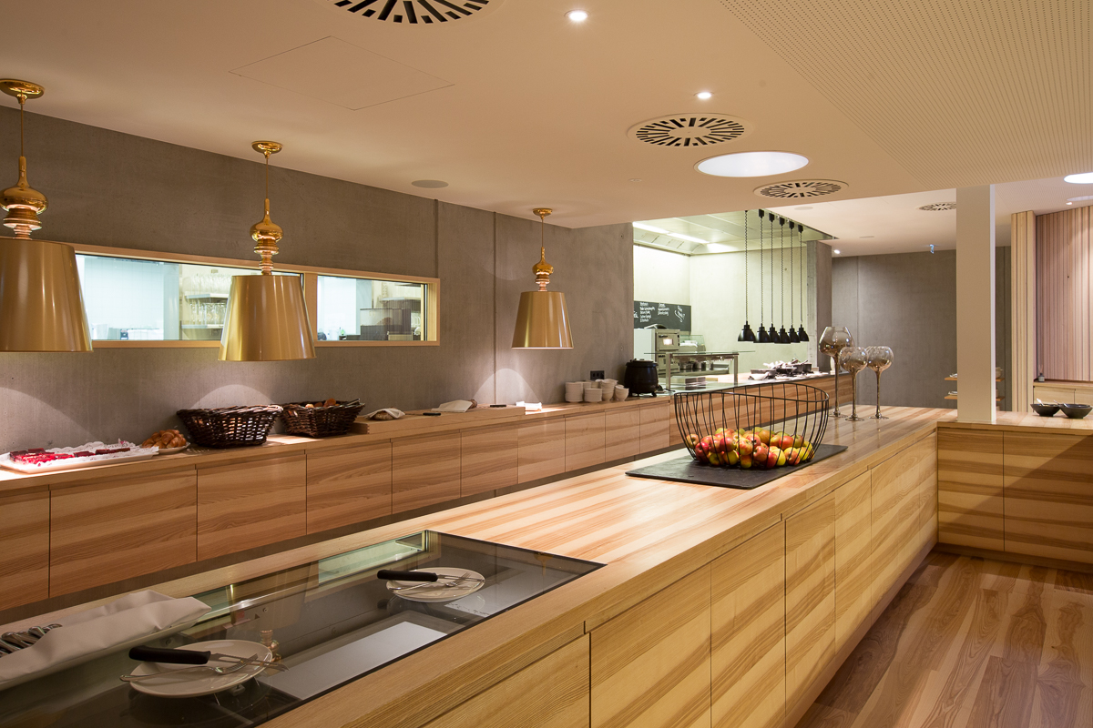 Ein stilvoll gestalteter Gastro-Bereich mit Holzregalen und modernen Lichtakzenten. Die Inneneinrichtung besticht durch ihre funktionale und gleichzeitig ästhetische Gestaltung. FHE GASTRO ist der führende Hersteller und Lieferant von Gastronomiemöbeln und -geräten, die den höchsten Standards für die Gastronomie entsprechen.