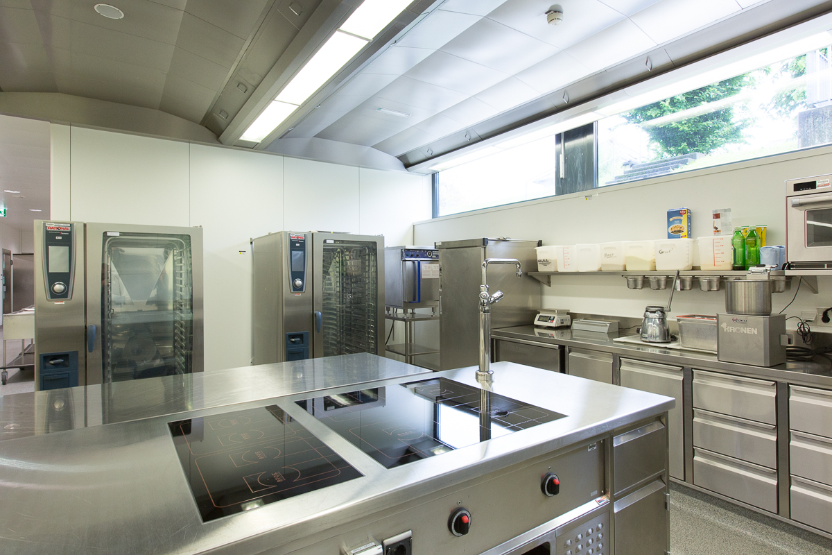 Blick auf eine professionelle Gastronomieküche mit einer modernen Kochstation, Induktionskochfeldern und Kombidämpfern. Die hochwertige Ausstattung von FHE GASTRO garantiert eine effiziente und hygienische Arbeitsumgebung für den Gastronomiebereich.