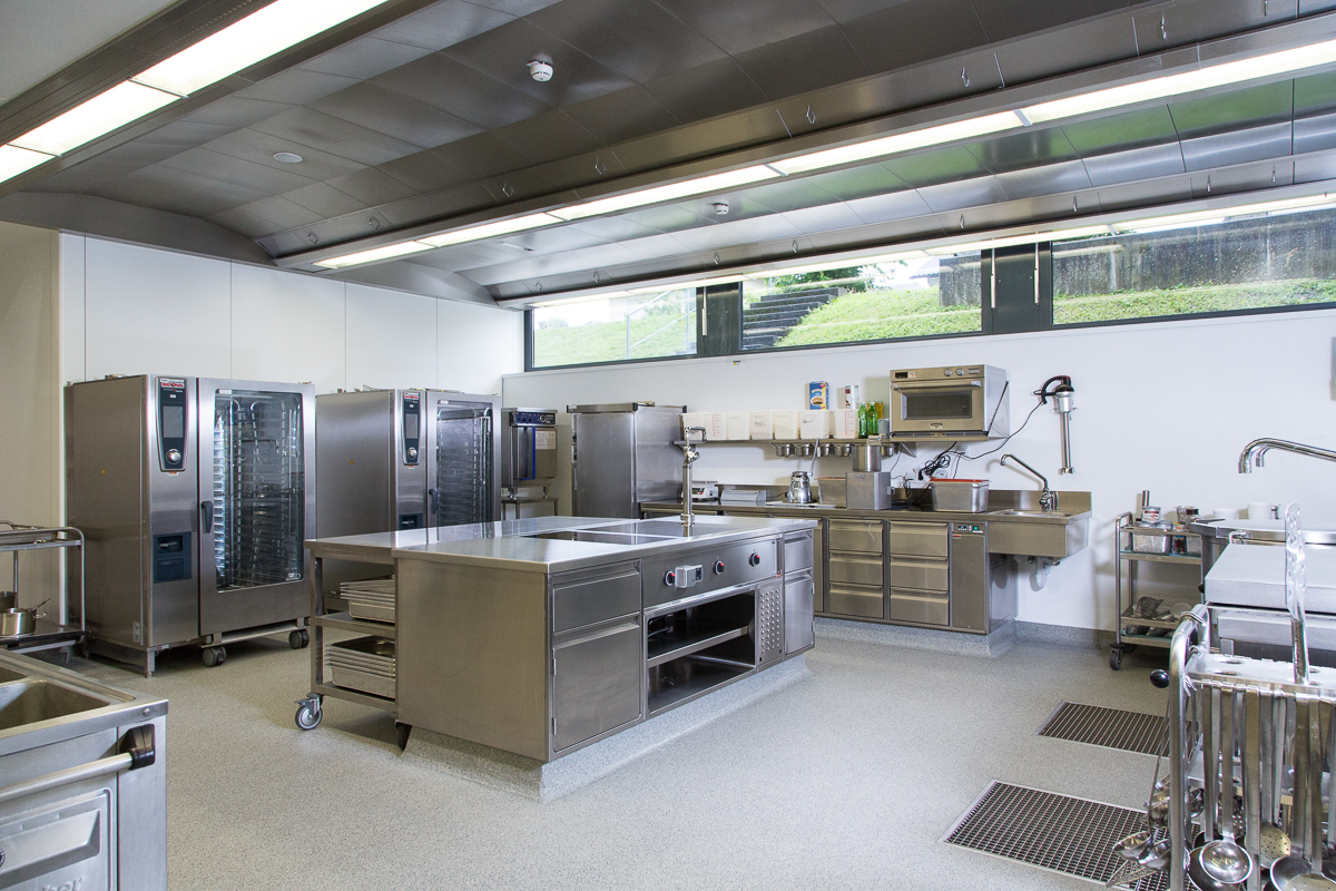 Blick auf eine professionell ausgestattete Gastronomieküche mit modernen Geräten wie Kombidämpfern, Edelstahl-Arbeitsflächen und praktischen Stauraumlösungen. Diese hochwertige Küchenausstattung von FHE GASTRO sorgt für eine effiziente Zubereitung von Speisen in Gastronomiebetrieben.