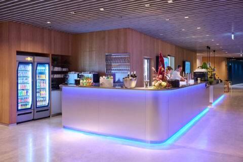 FHE GASTRO Barbereich mit modernem, funktionalem Design. Die elegante Theke ist ausgestattet mit Zapfanlagen und einer ansprechenden Auswahl an Getränken. Kühlvitrinen präsentieren die Getränkeauswahl, während freundliche Mitarbeiter den Service bereitstellen.