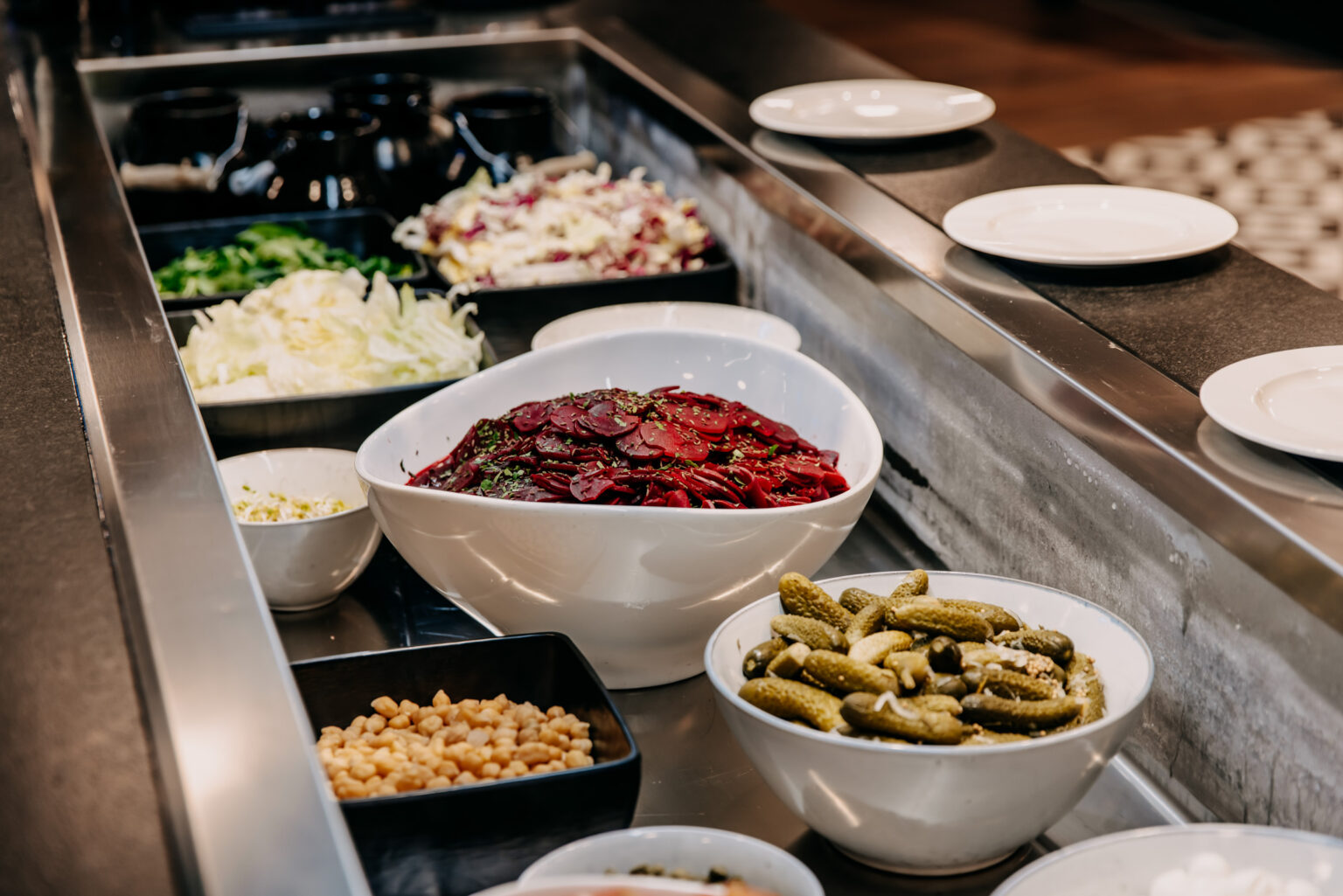231226_Campus_forsthofgut-218 Buffetbereich mit verschiedenen Salaten und Beilagen in ansprechender Präsentation. Die moderne Einrichtung und die funktionalen Möbel schaffen ein angenehmes Erlebnis für Gäste. FHE GASTRO bietet maßgefertigte Lösungen für Selbstbedienungsstationen, die sowohl ästhetisch als auch praktisch sind.