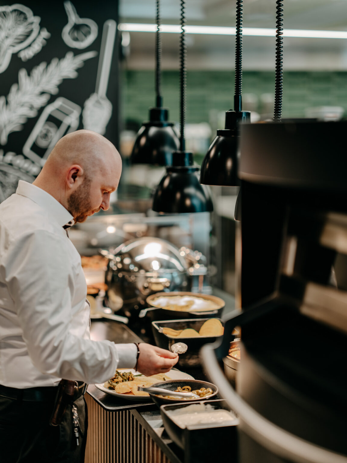 240312_Forsthofgut_patrese-136 Ein gastronomischer Bereich mit einem Buffet und einem Koch, der eine frische Mahlzeit zubereitet. Die moderne Ausstattung aus Holz und Edelstahl sowie die stilvolle Beleuchtung bieten eine angenehme Atmosphäre für Gäste. FHE GASTRO liefert funktionale und ästhetische Lösungen für die Gastronomie, die den höchsten Standards entsprechen.
